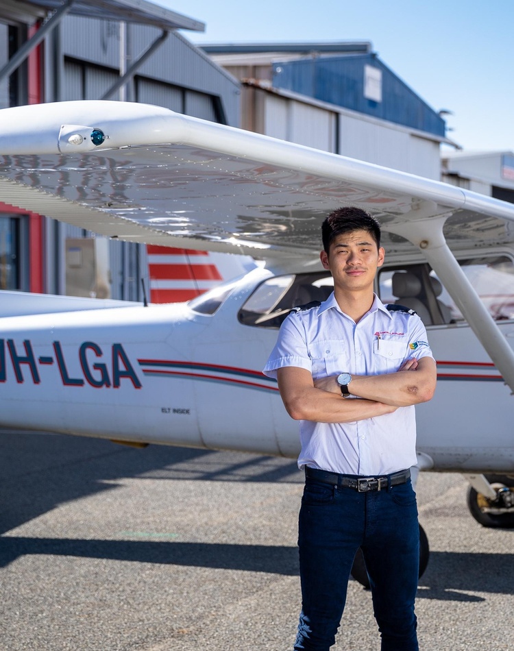 An international student stands in front of small plane at airport