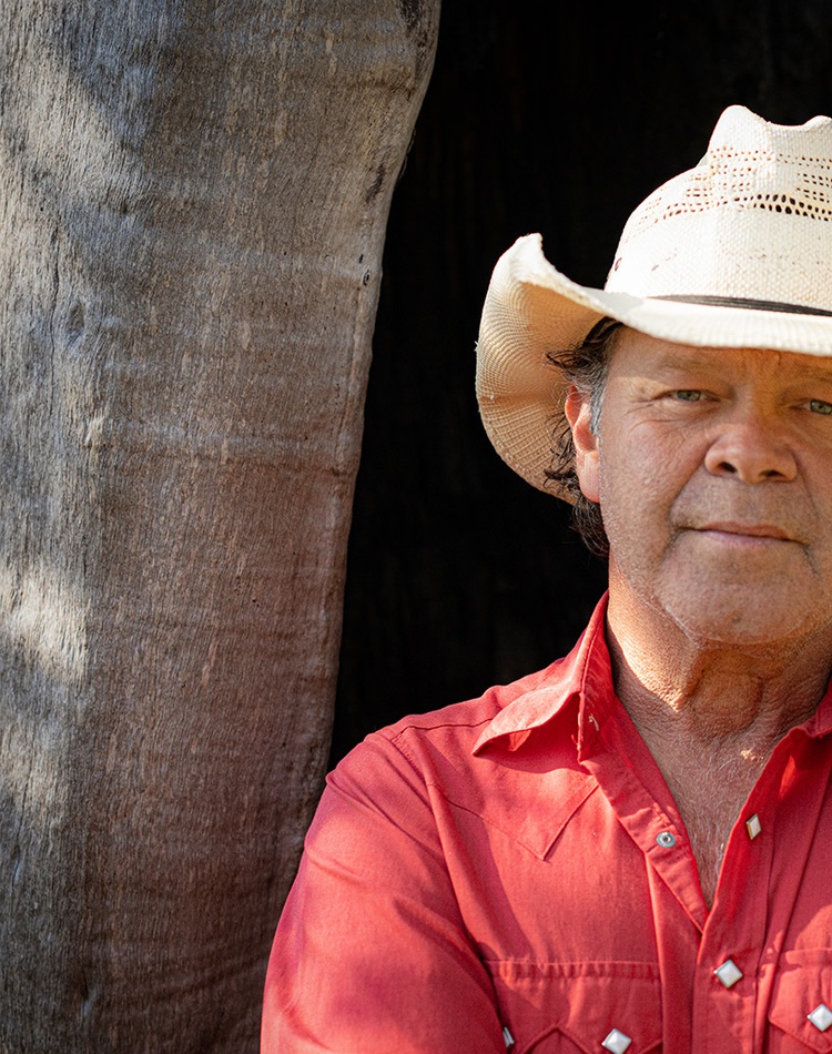 Man in cowboy hat standing in front of large tree trunk