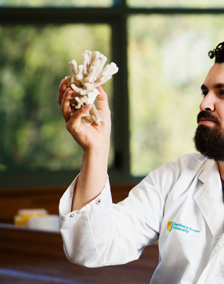 A student in a lab coat examining a piece of coral.