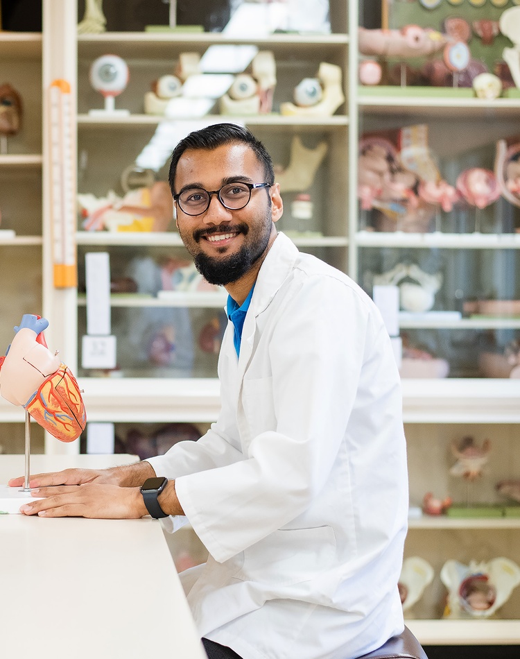 Arpan Kuwar an international student studying Nursing wearing a white lab coat and sitting in a lab looking a model of a heart at Southern Cross University Lismore Campus