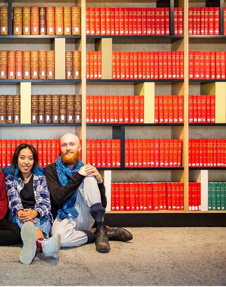 5 people sitting on floor leaning against large book shelf