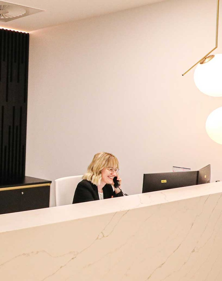 Woman sitting at reception desk with The Hotel School Brisbane sign in background