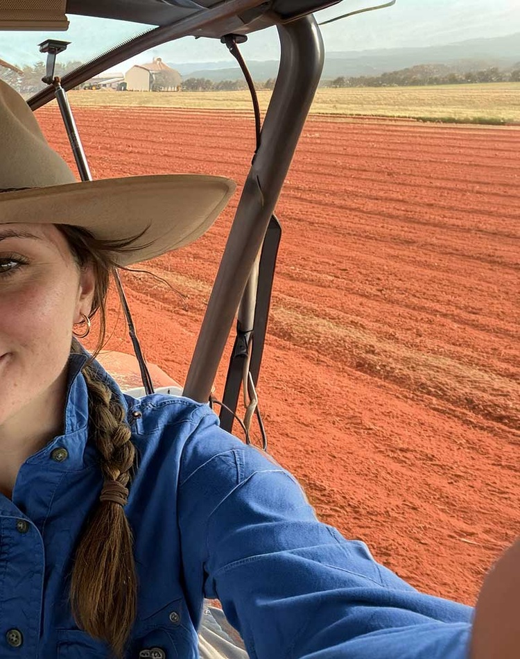 Girl in a hat smiling at camera in tractor with red dirt behind