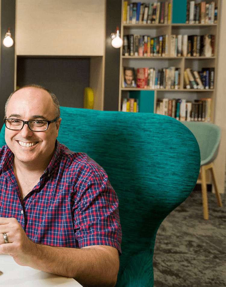 Professor Mark Hughes sitting at table with laptop and smiling