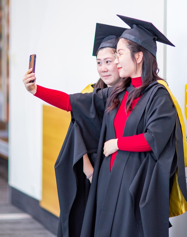 Two student posing for a selfie in graduation attire