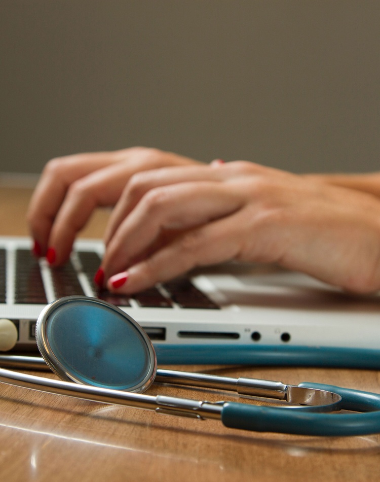 student typing on laptop with stethoscope on side