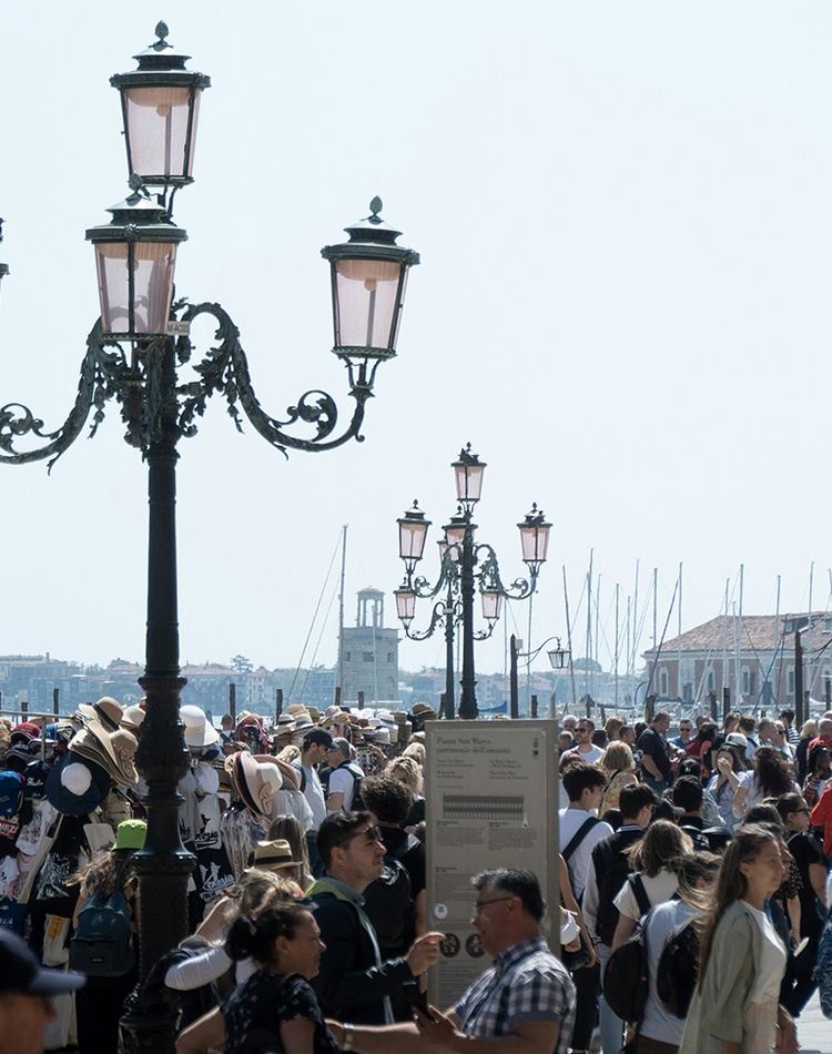 A bustling city square filled with people overlooking a waterway