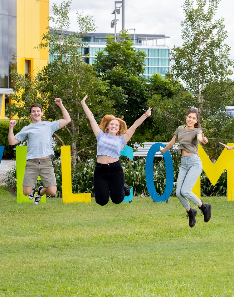Students jumping in the air with large welcome sign in background