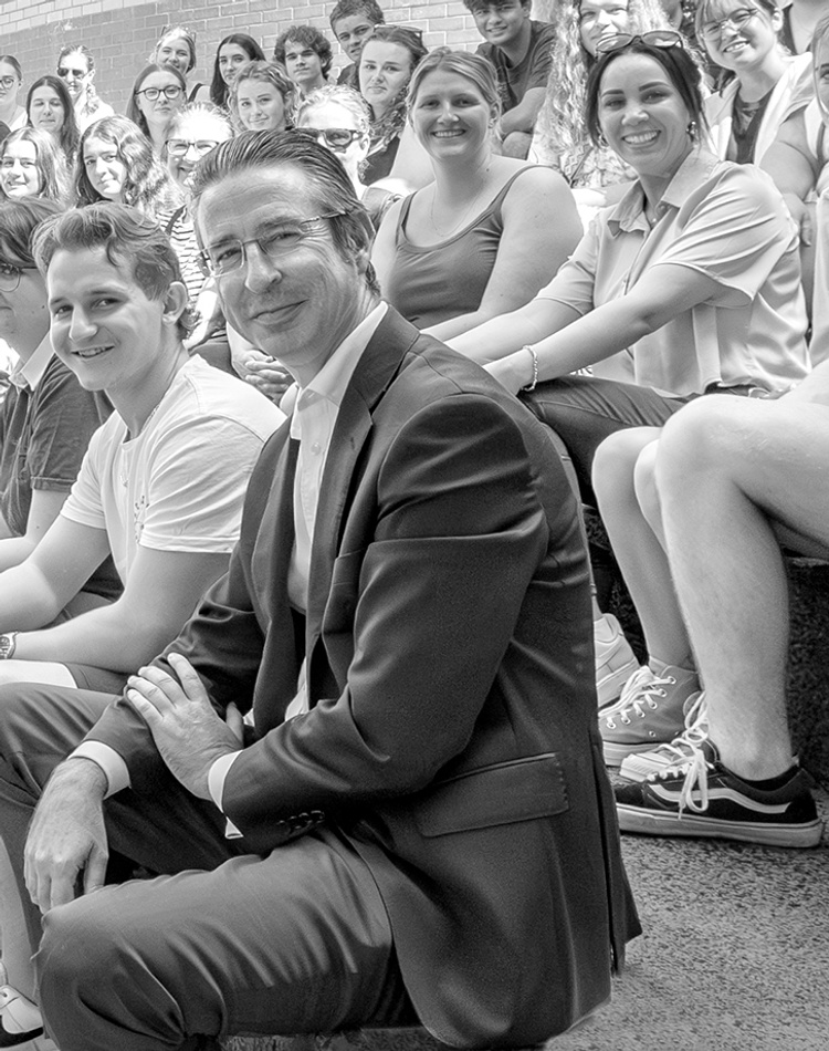 A large group of students and the Vice-Chancellor sitting on concrete steps facing the camera