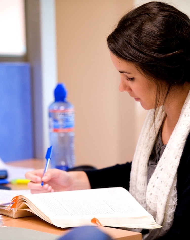 A student doing research at a desk with pen and paper