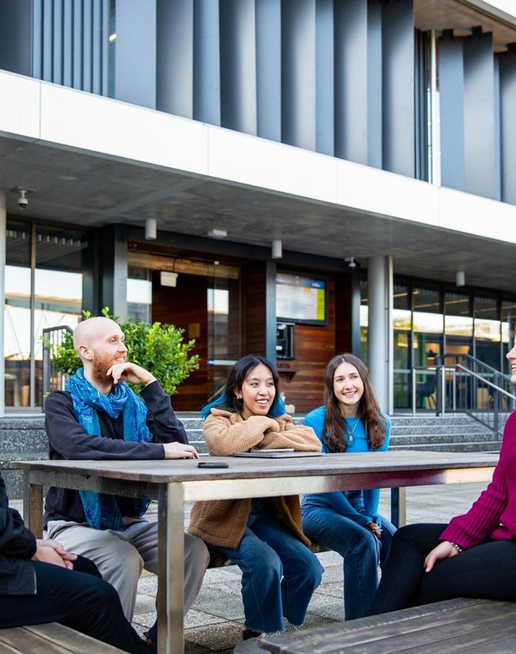A group of students sit together and chat at an outdoor table.
