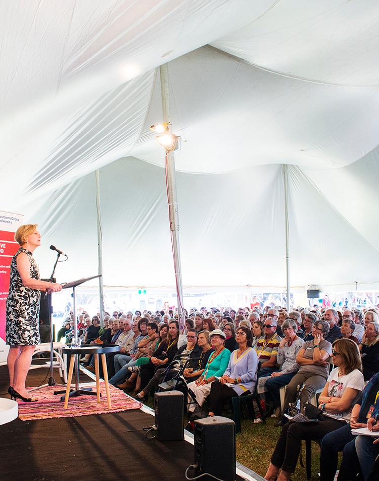 A woman addresses a large group of people under a marquee