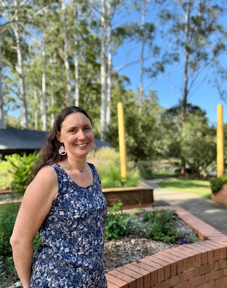 A woman standing in a garden of herbs, trees in the background