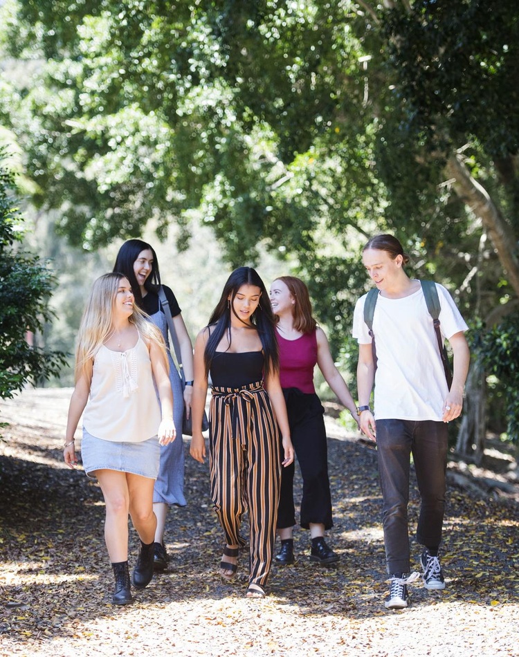 Young group of students walking through a leafy green path talking and smiling