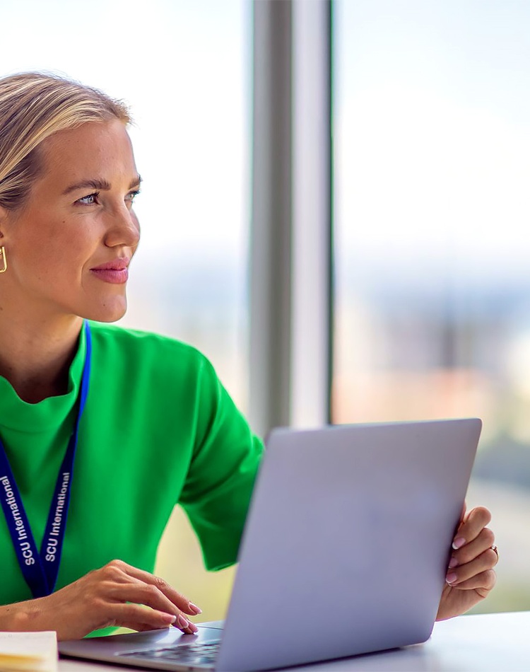 A female student sitting at a desk with a laptop she is looking off camera to the side