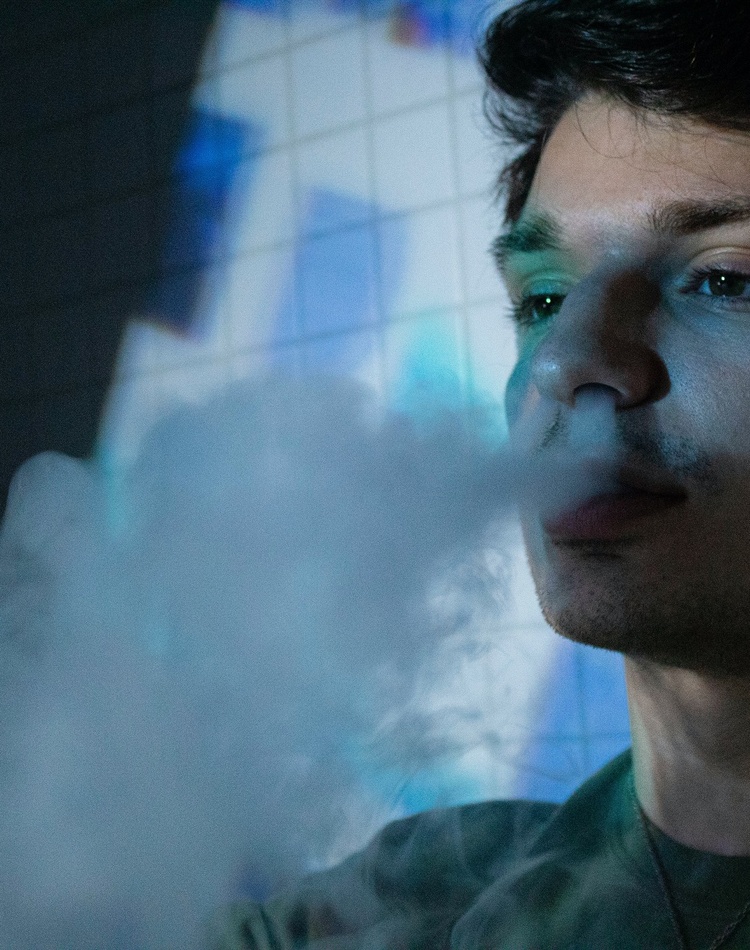 A young man blowing smoke from an e-cigarette