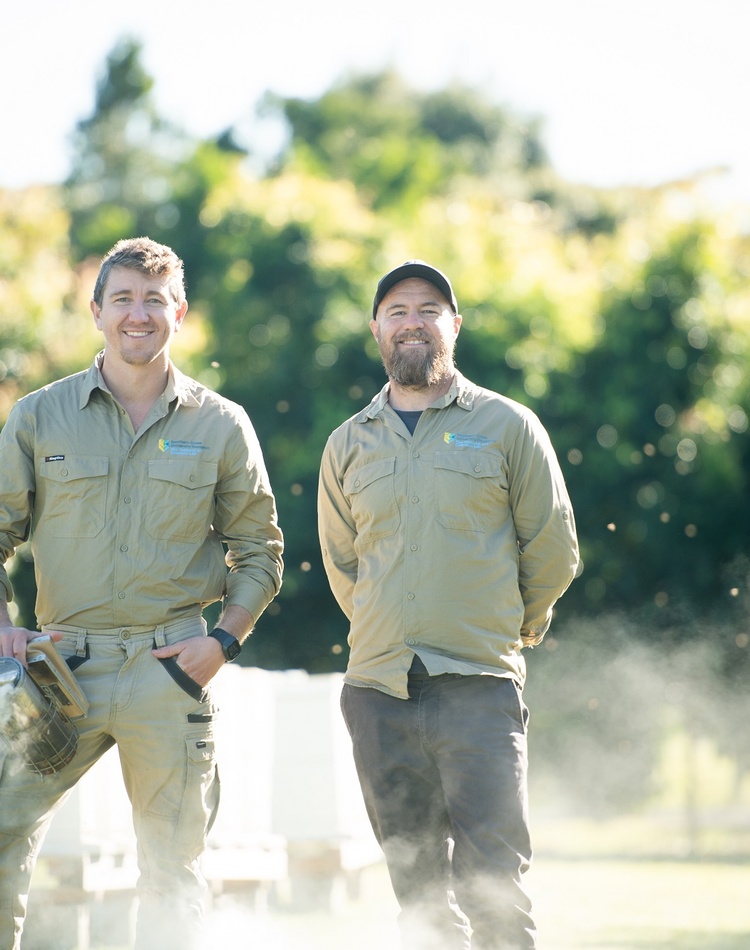 Two men in a field with bee hives in the background