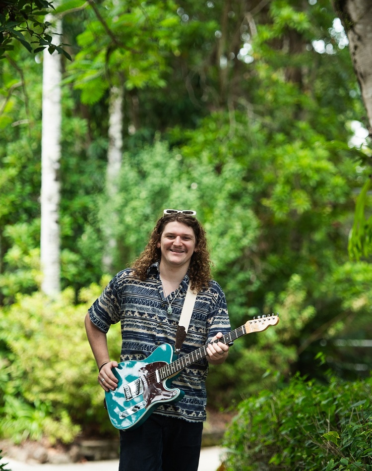 A man with a guitar in a green leafy setting