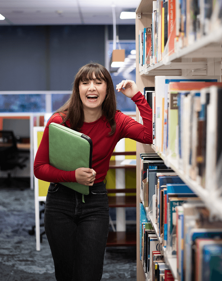 Student in Library surrounded by books on shelf