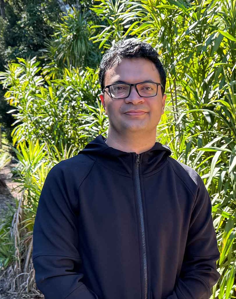 Suman Regmi standing in front of greenery wearing black jumper