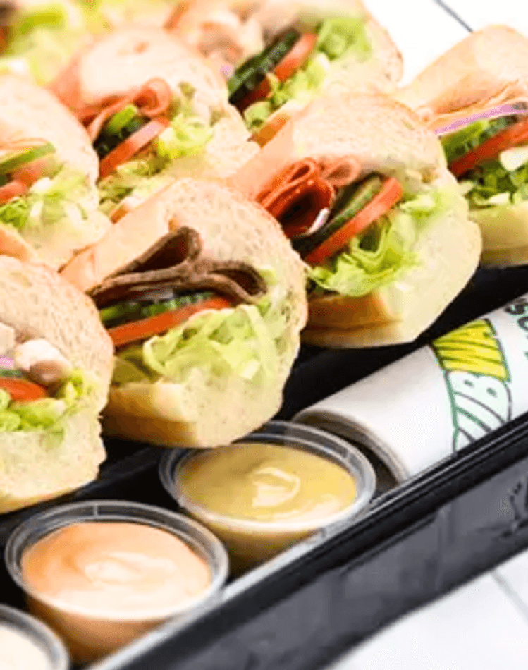A tray of subway sandwich rolls with salad and dips