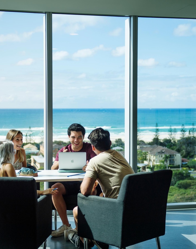 Four students sitting at a table studying with the ocean in the background