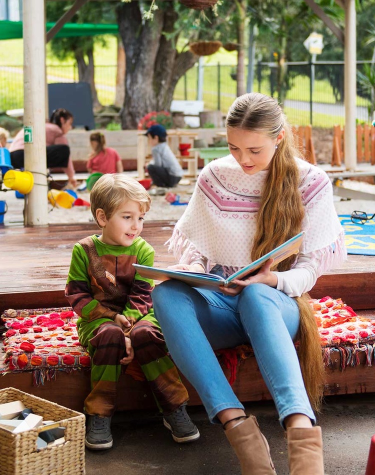 Early Childhood teacher reading with pupil in playground