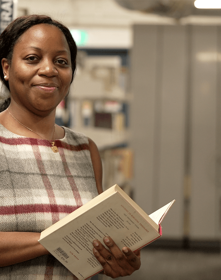 Professor Ebi Cocodia holding open book in library