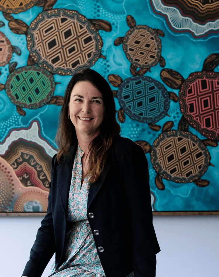 Doctor of Indigenous Philosophies graduate Kylie Day sitting in front of painting