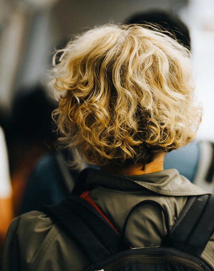 Back of head of someone with curly blonde hair wearing a backpack