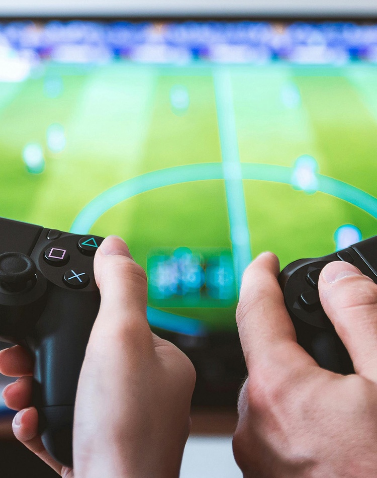 Twos sets of hands holding PlayStation 4 controllers with tv with sports game in background