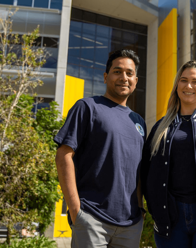 Man and woman smiling at camera in front of yellow building