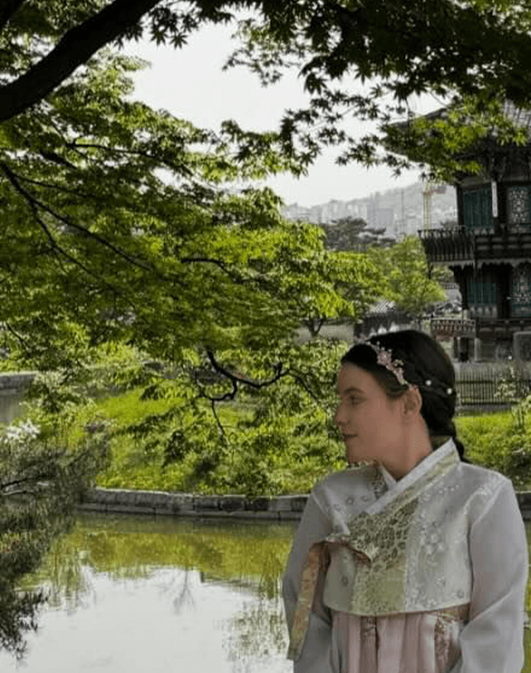 Student in traditional Korean attire in front of river and temple