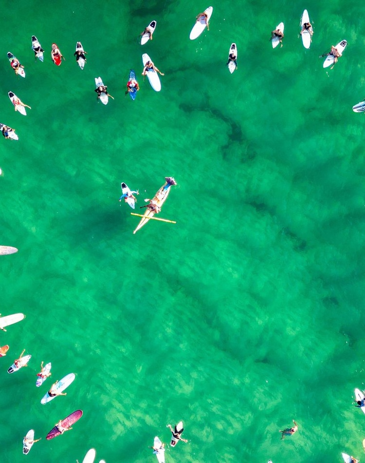 Aerial shot of surfers on surfboards forming a love heart in the ocean