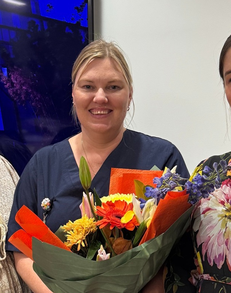 Three women smiling, the middle person holding bouquet of flowers
