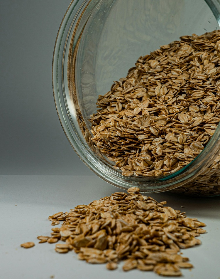 A glass jar of oats spilling onto a white counter