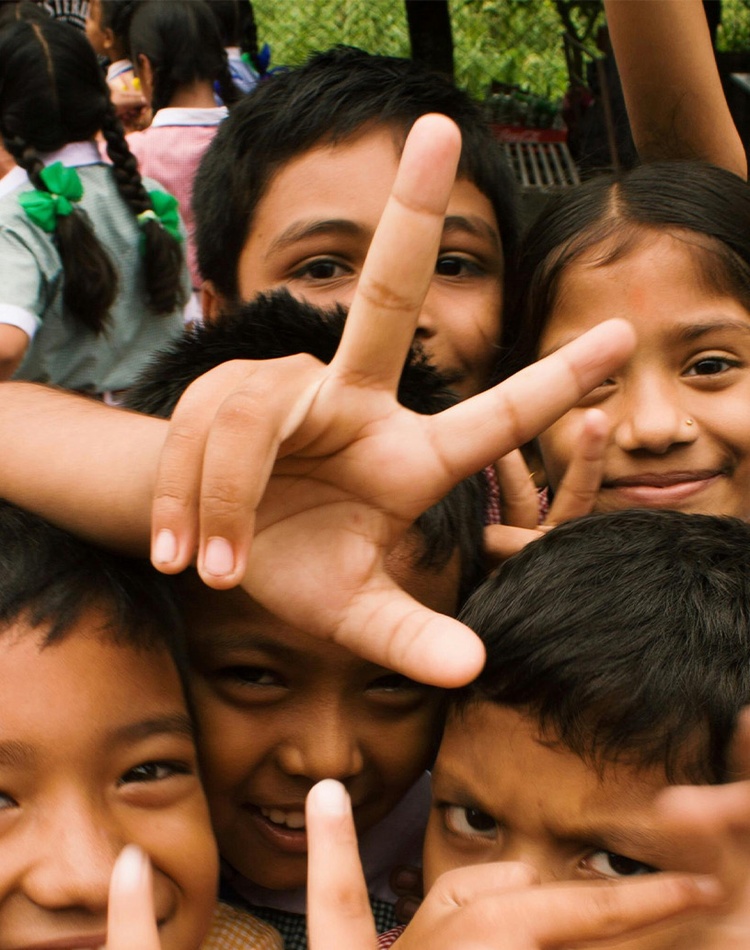 A group of young children crowding camera and holding hands up