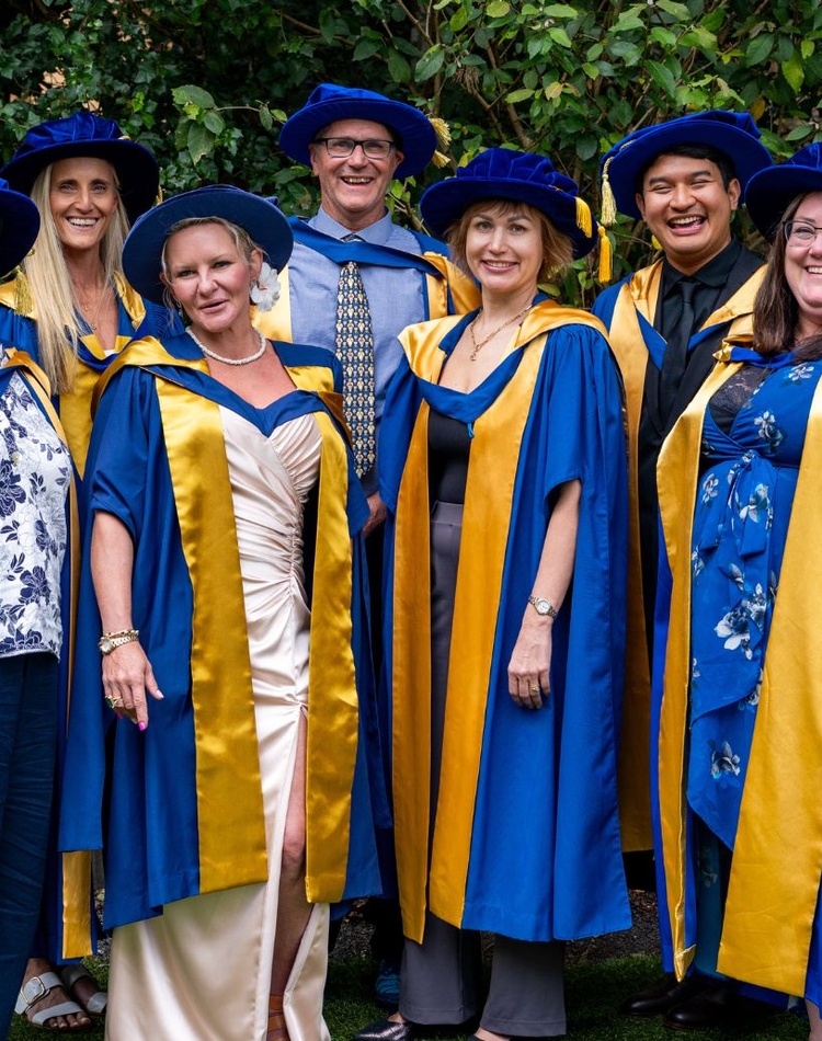 Graduates standing in a group in graduation robes smiling at camera