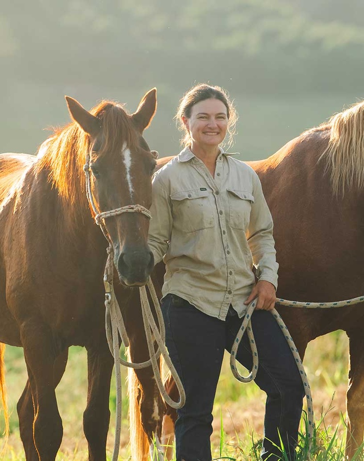 Student standing in paddock with two horses