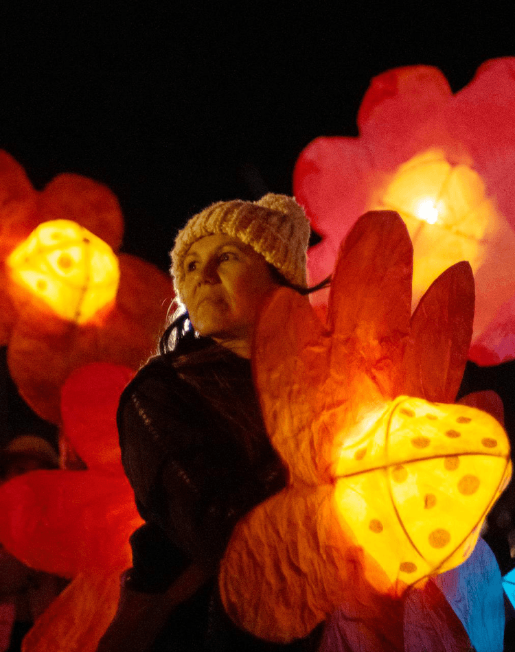 Woman in beanie holding lantern while other flower lanterns float around her