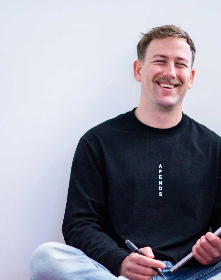 Nathan smiling sitting cross-legged with notebook and pen
