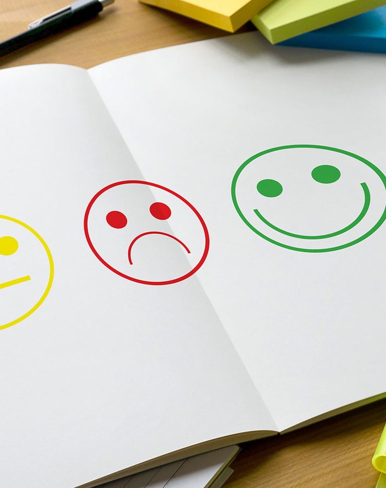 yellow neutral, red unhappy and green smiley face drawings on a white page with highlighter pens, post-its and devices surrounding