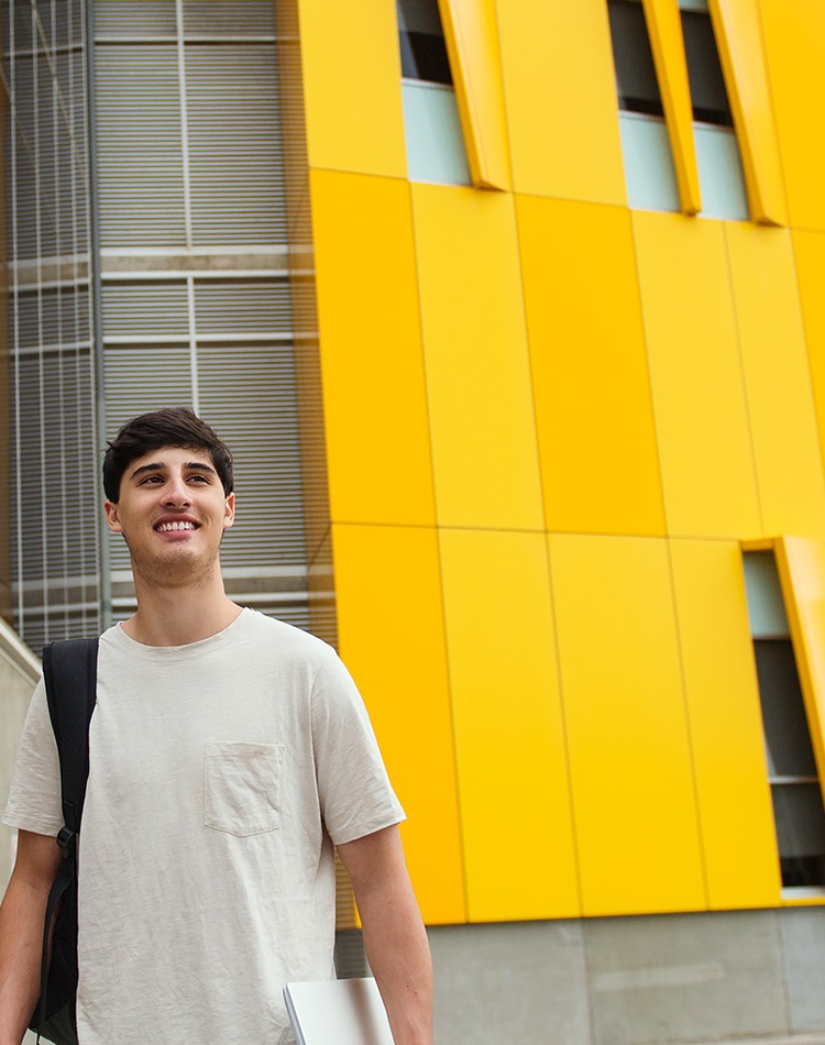 An international student is smiling away from the camera. He is wearing a white t shirt and is at the Southern Cross University Gold Coast campus