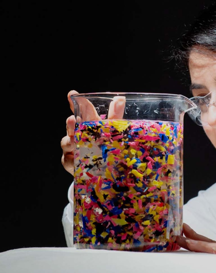 A researcher looks into a beaker full of brightly coloured plastics