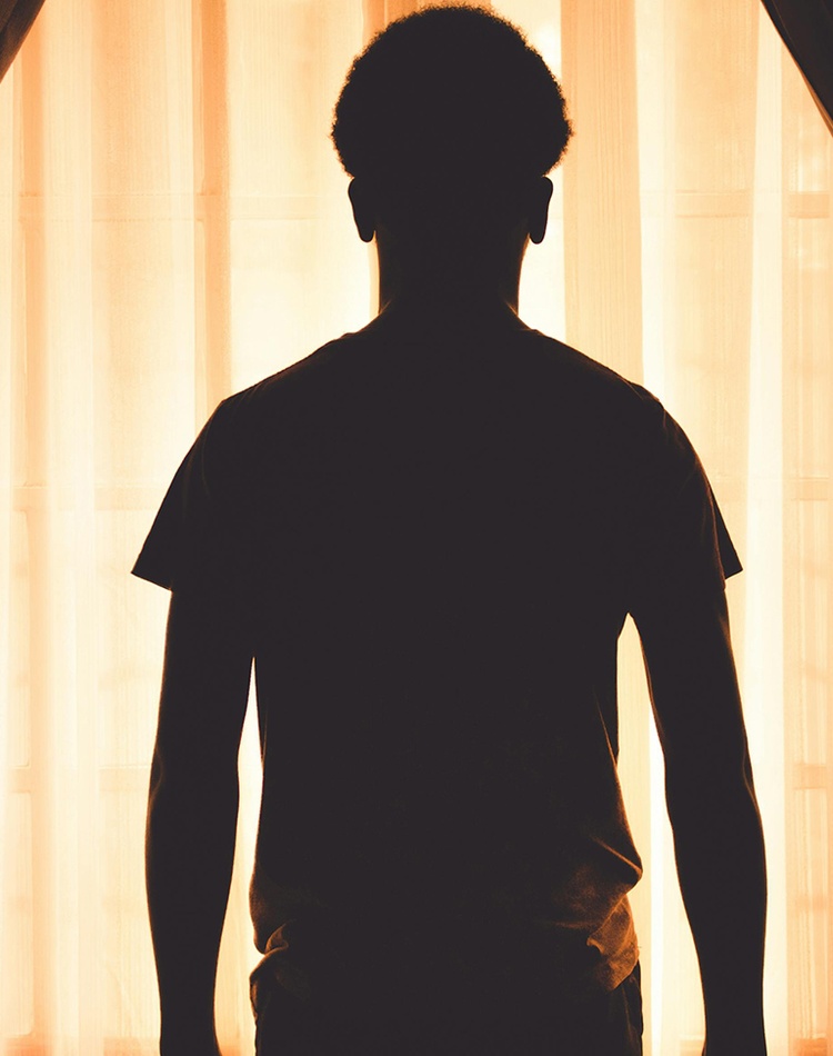 Silhouette of a boy standing against curtains in a dark room