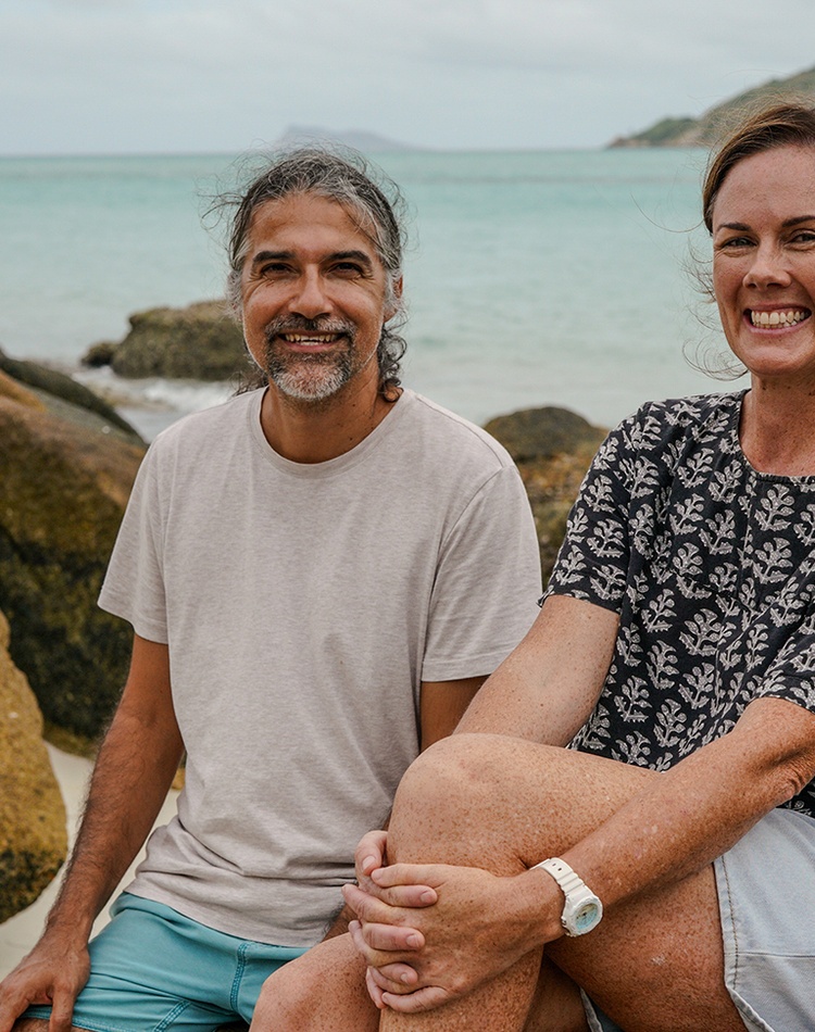 A man and woman sitting on rocks with the ocean and an island in the background