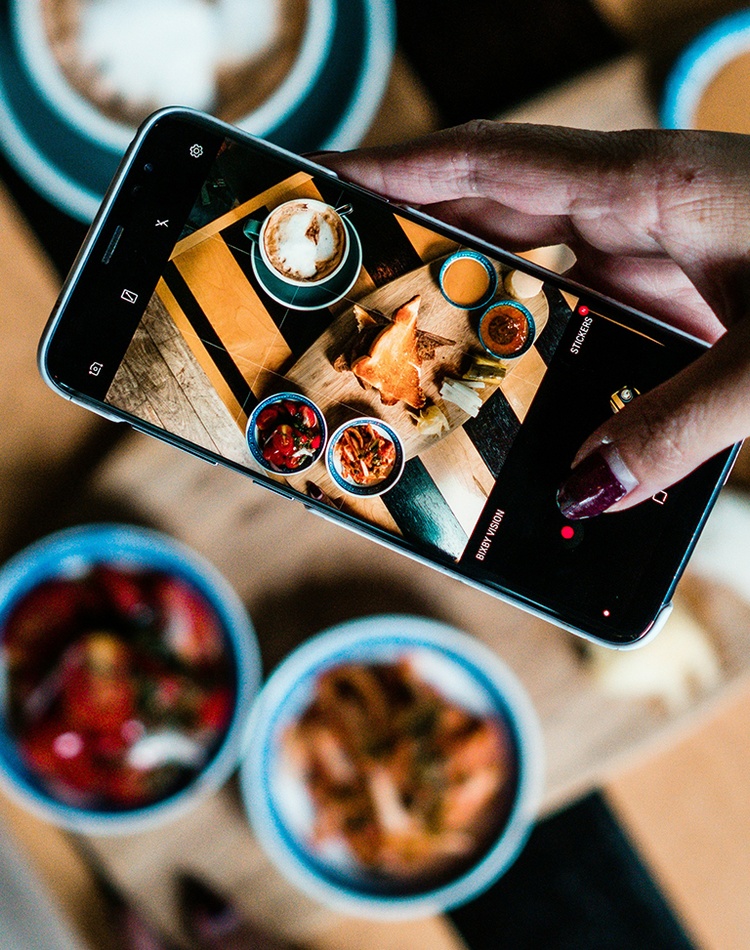 Person with a mobile phone takes a photo of the food on a table.