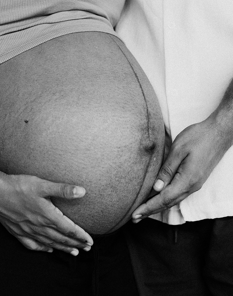 A black and white image of the belly of a pregnant women with male partner touching her belly