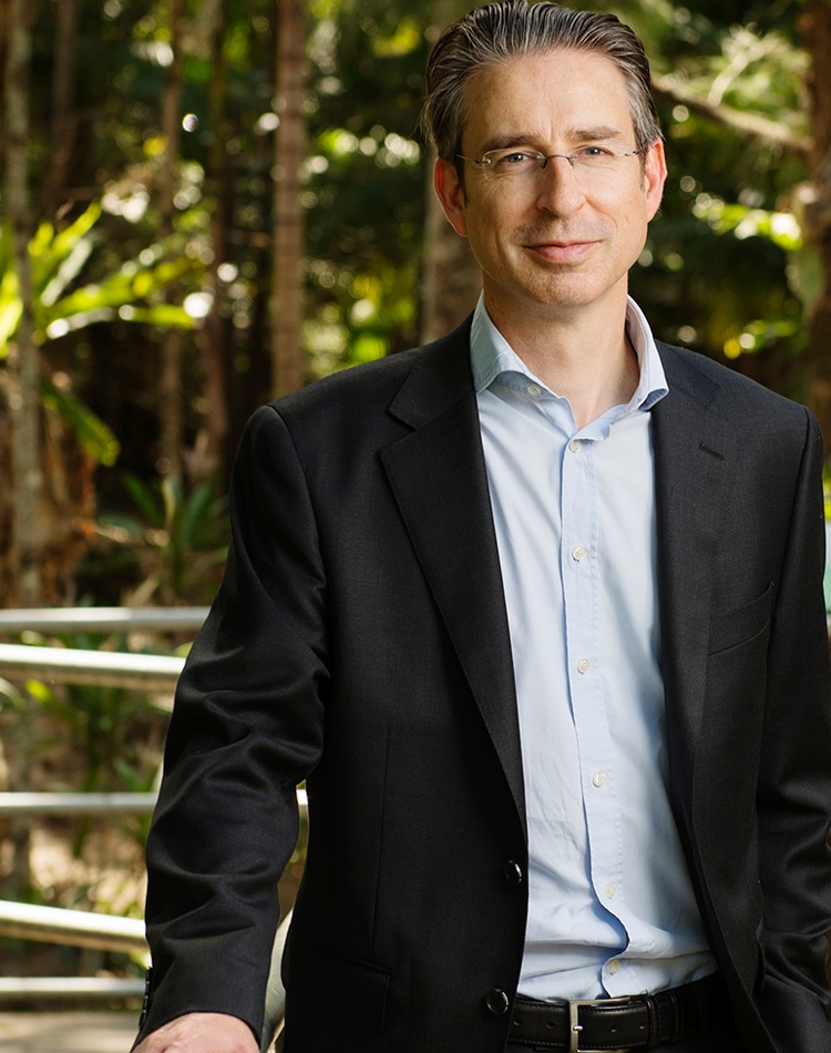 A man in a business suit and open shirt standing outside in a garden.