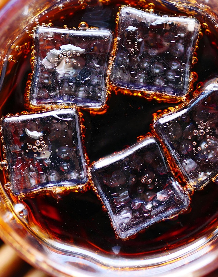 A dark-coloured soft drink in a glass with ice